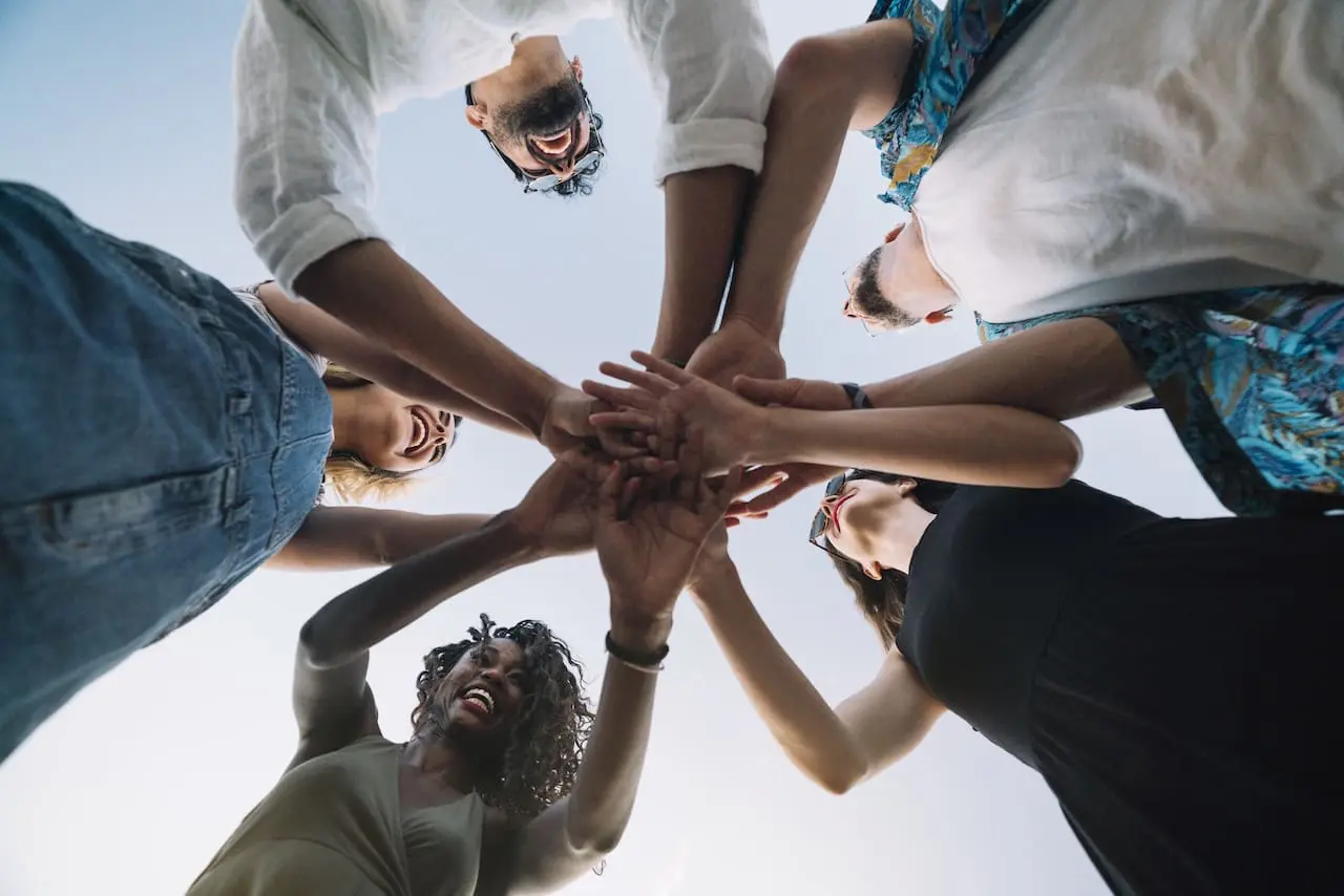 Excited coworkers standing in a circle putting their hands together in a circle before volunteering for the community